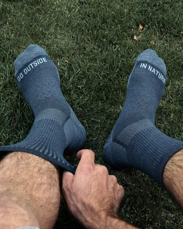 Man Putting on Charcoal Blue Trail Alpaca Wool 3/4 Crew Socks from Above with “Go Outside in Nature” Text – PAKA Apparel