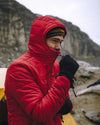 Man Zipping Up Apu Oxblood / Red Alpaca Midweight Puffer Jacket with Hood Up in Front of Rock Wall – PAKA Apparel