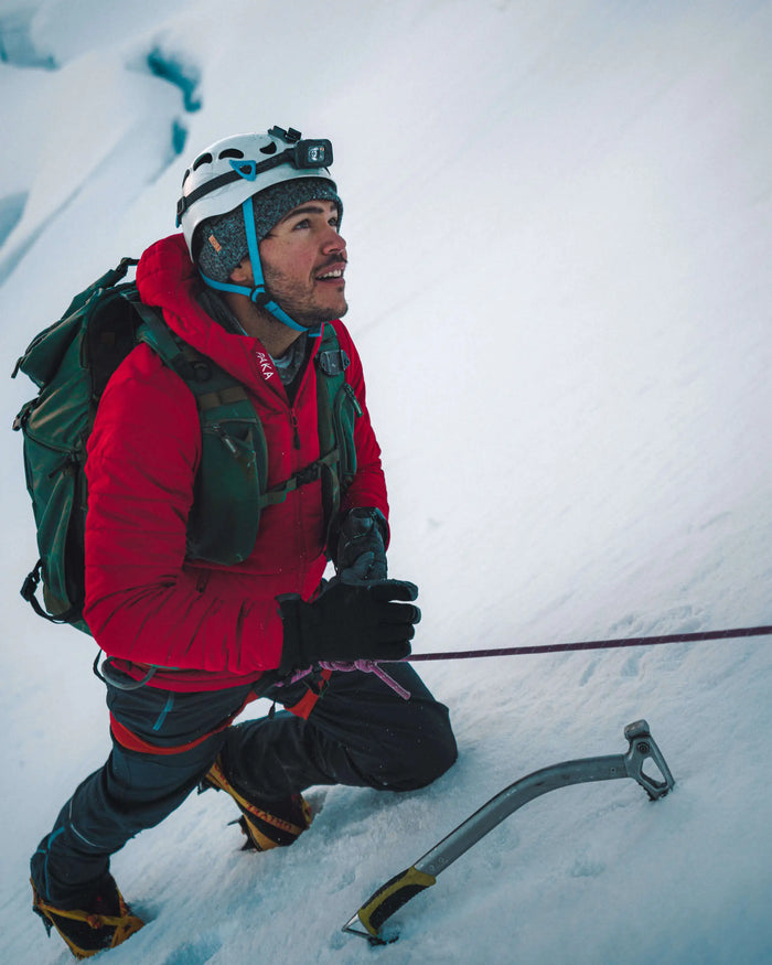 Summiting a mountain in red puffer jacket with rope and pick axe 