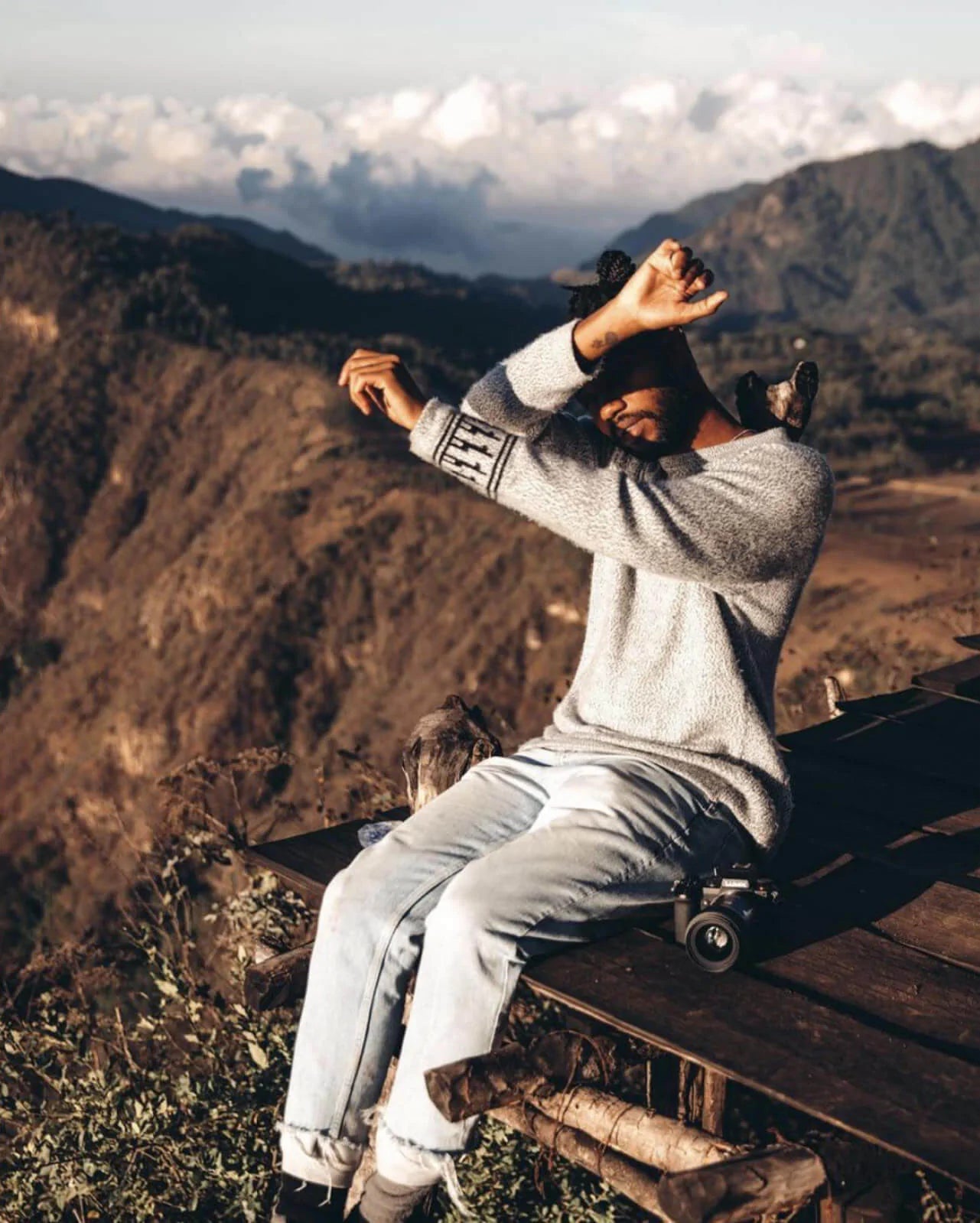 Man Sitting on Platform Wearing The Costa Alpaca Sweater Blocking Sun from Eyes with Mountains in Background - PAKA Apparel