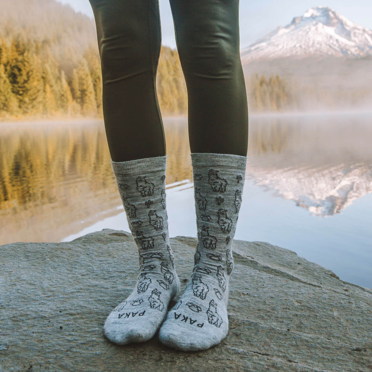 Person’s Standing Feet in Light Grey Alpaca Wool Crew Socks in Front of Lake with the Reflection of a Mountain – PAKA Apparel