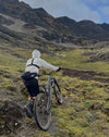 Man Walking with Mountain Bike Towards an Alpaca Herd in Mountains While Wearing Alpaca Wool Outdoor Clothing – PAKA Apparel