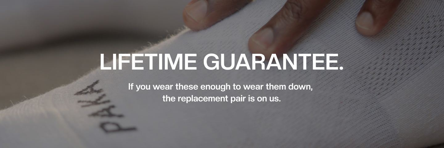 Text Reading “Lifetime Guarantee. If you wear these enough to wear them down, the replacement pair is on us” with Hand on White Alpaca Wool Sock in Background