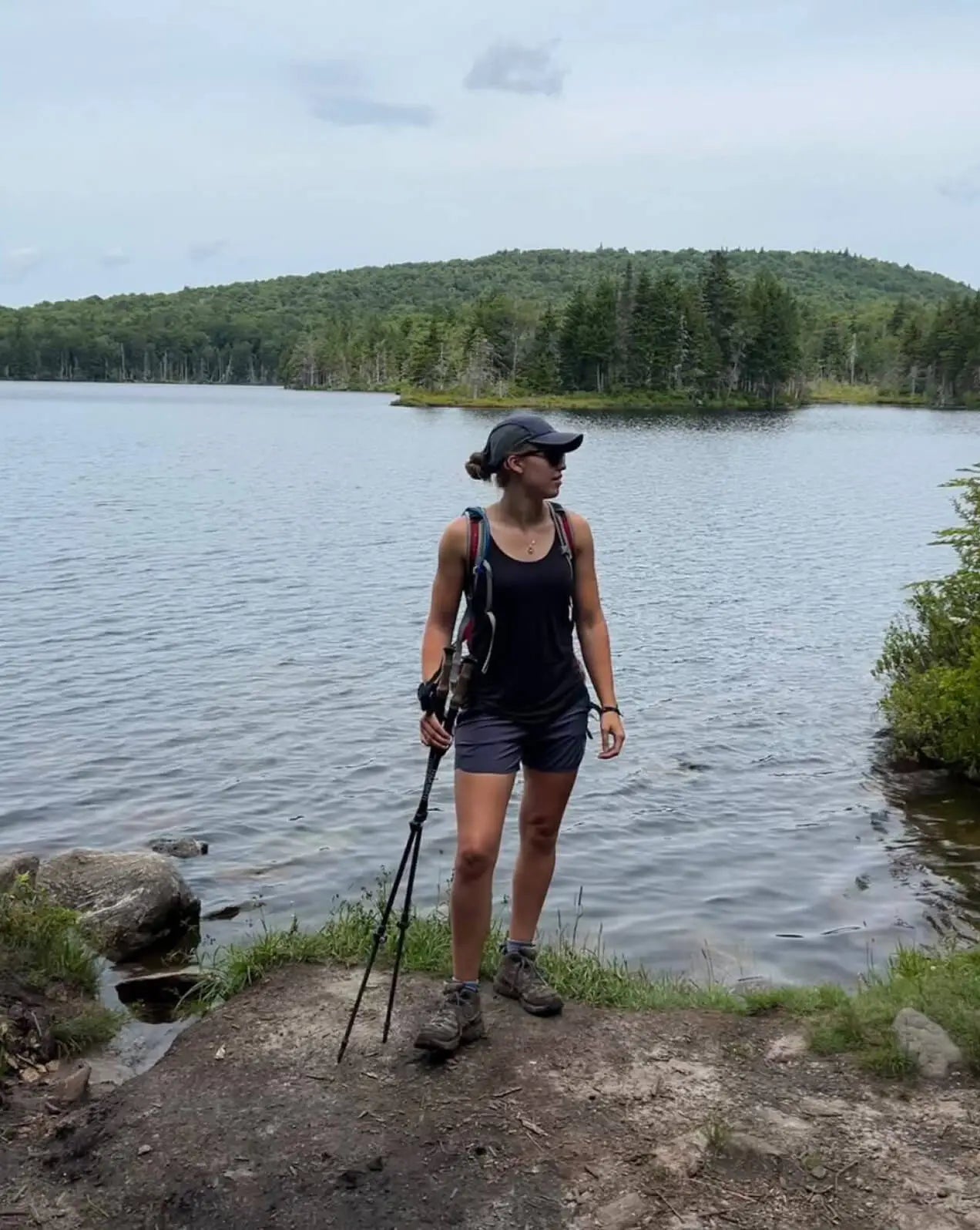 A woman wearing a black alpaca racer tank in front of a lake