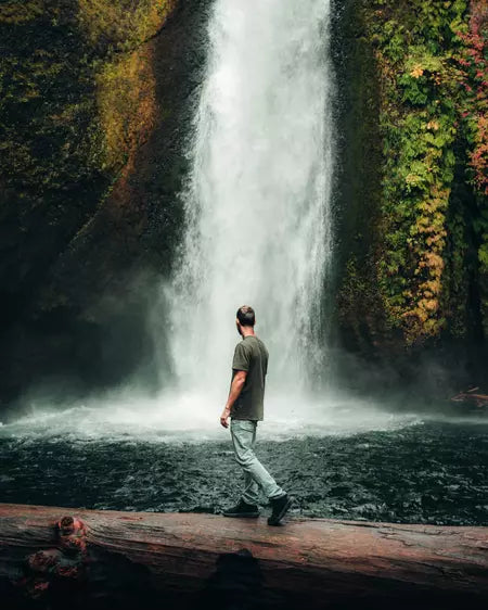 Man Walking Across Fallen Tree in Front of Waterfall Wearing Green Lightweight Alpaca Blend T-Shirt - PAKA Apparel