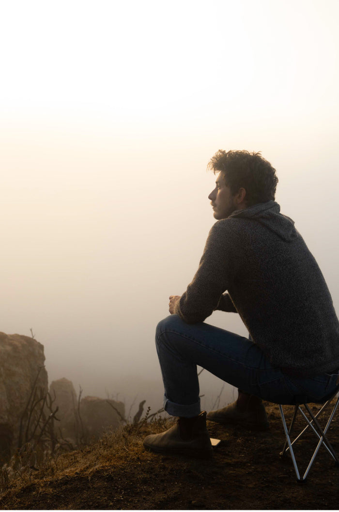 Man Sitting on Camp Chair in Mist Wearing The Vida Alpaca Wool Hoodie for Hiking and Outdoors – PAKA Apparel