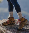 Woman’s Legs Wearing Sebastian the Alpaca Graphic Odor-Resistant Alpaca Wool Socks Over Tights with Hiking Boots on Mountain Top - PAKA Apparel