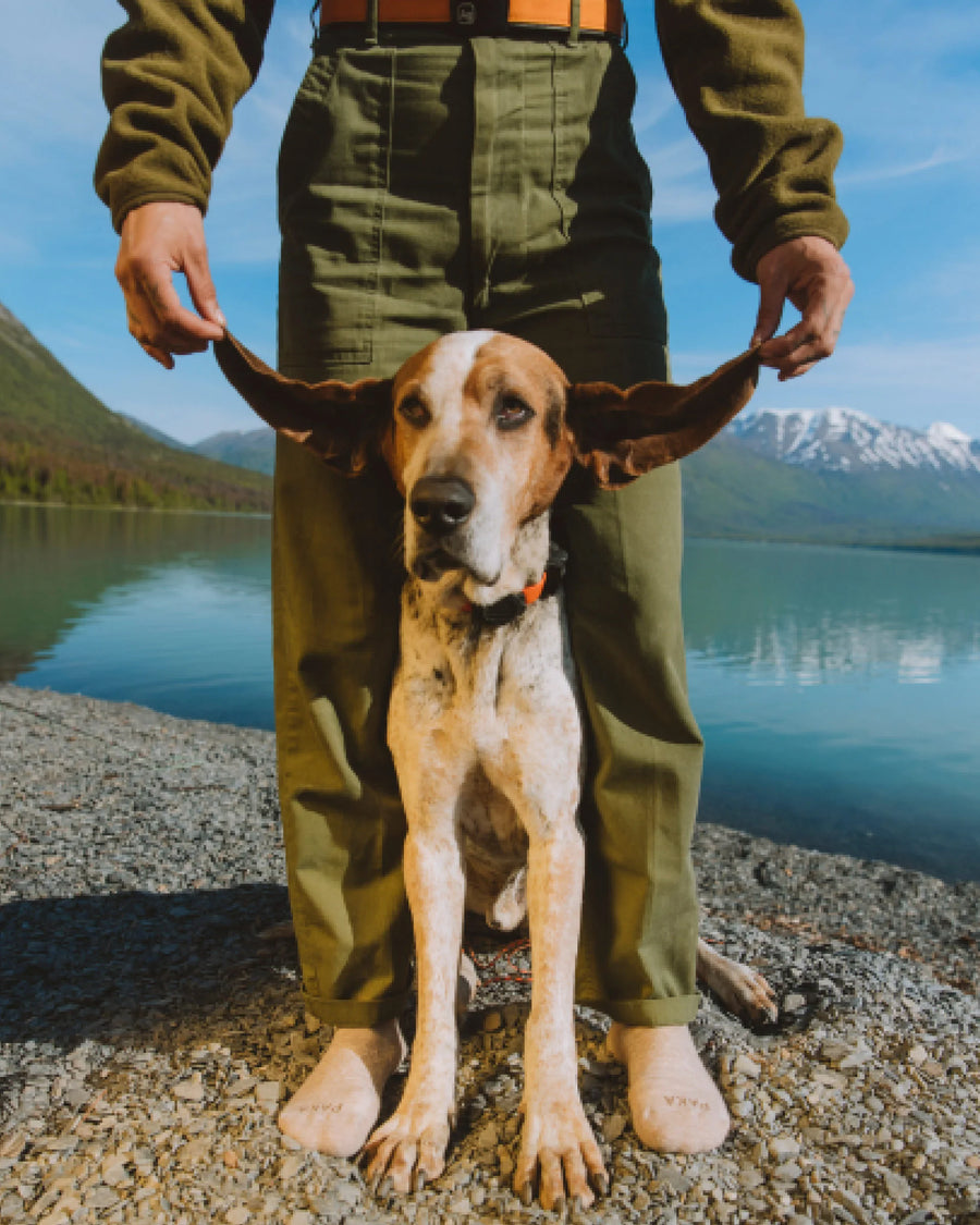 Man Wearing Timber / Tan Alpaca Ankle Socks While Holding Dog’s Ears in Front of Mountain Lake – PAKA Apparel