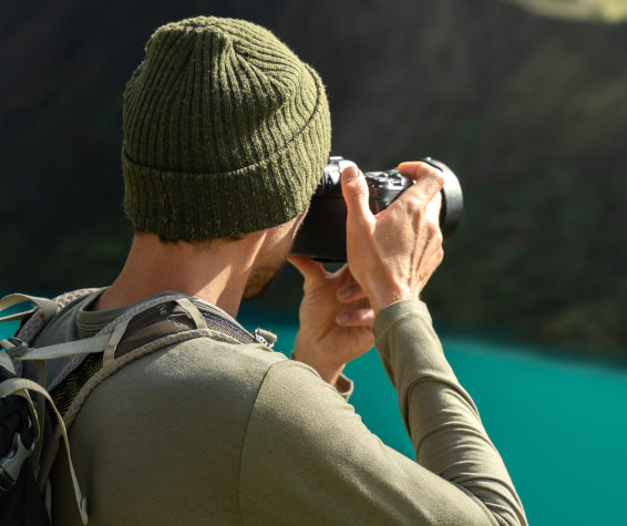 Man in Lightweight Alpaca Wool Baselayer Taking Picture with Camera in Front of Blue Lake - PAKA Apparel