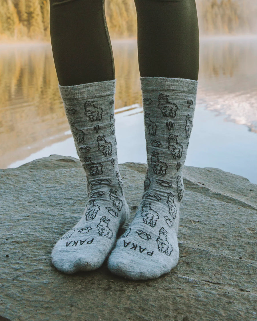 Light Grey Sebastian the Alpaca Pattern Graphic Alpaca Wool Socks Worn Over Tights in Front of Mountain Lake – PAKA Apparel on Woman Model