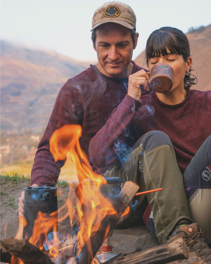 Man and Woman Sitting by Campfire Wearing Burgundy Dark Red The Cusco Alpaca Wool Crewneck Sweaters – PAKA Apparel