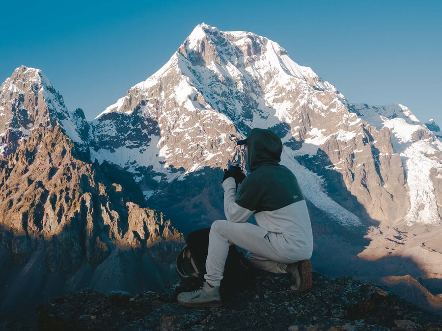 Man wearing green and tan alpaca hoodie over looking mountain 