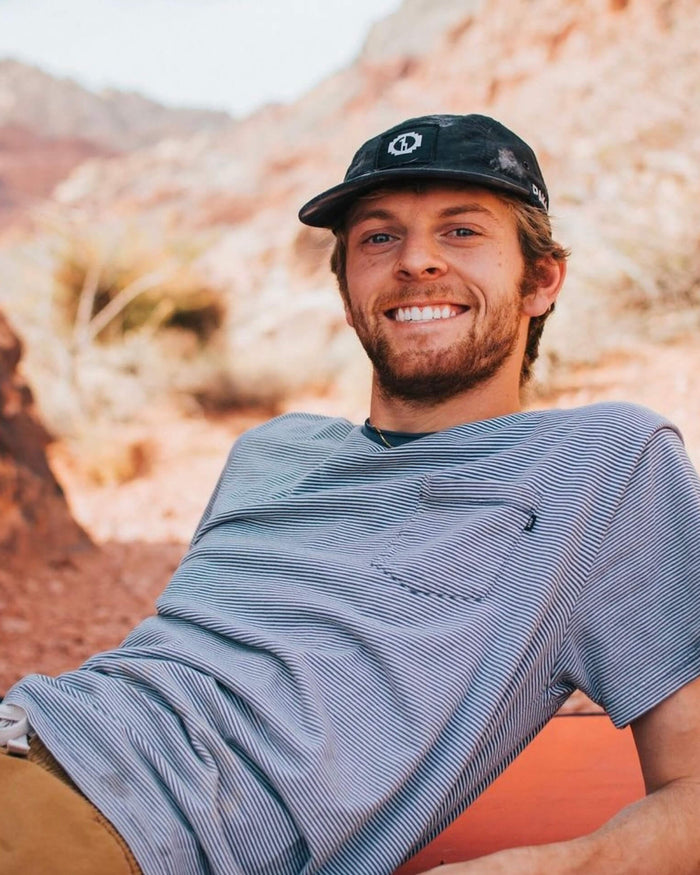 Man Smiling While Resting in Desert Wearing Black 5-Panel Hat / Cap with PAKA Logo on Front – PAKA Apparel