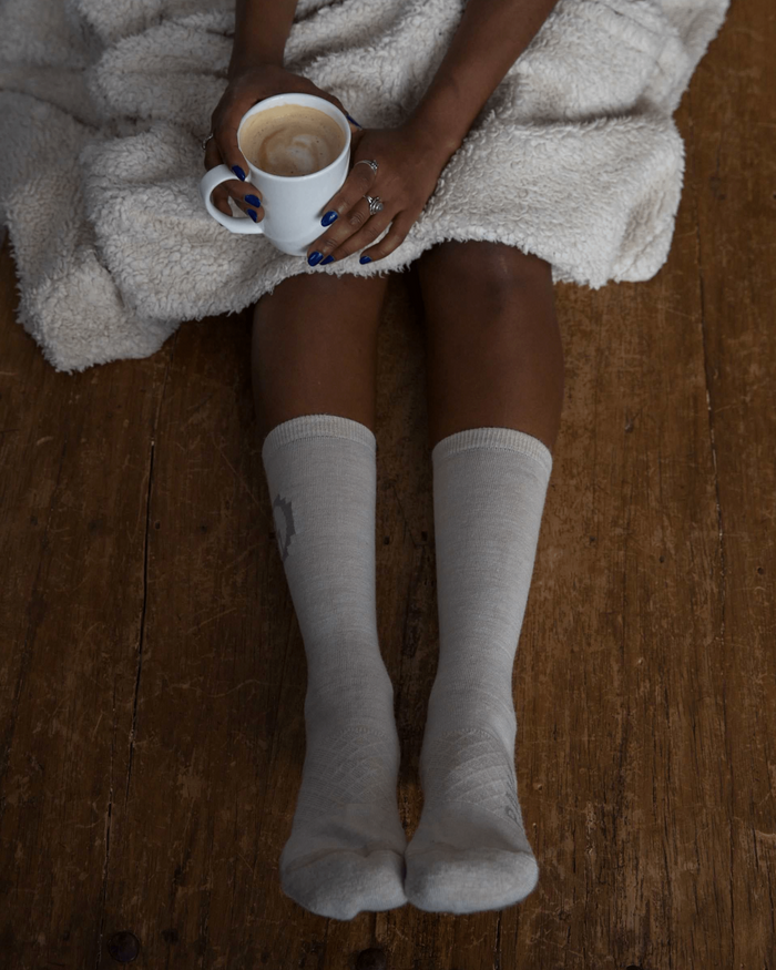 Ivory / Off White Alpaca Wool Crew Socks on Woman’s Legs on Floor with Coffee and Blanket on Lap - PAKA Apparel