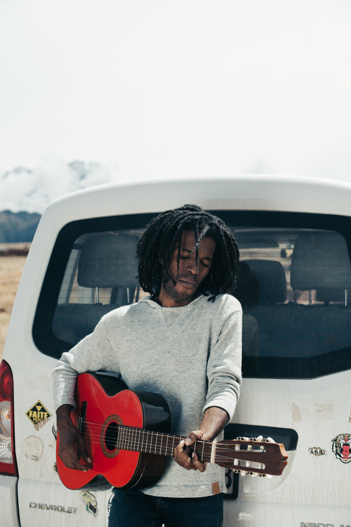 Male Model playing guitar behind car in Paka Hoodie