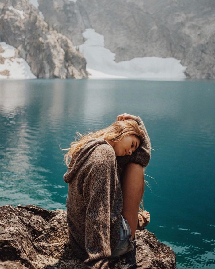 Woman sitting in front of blue lake wearing the Vida sweater