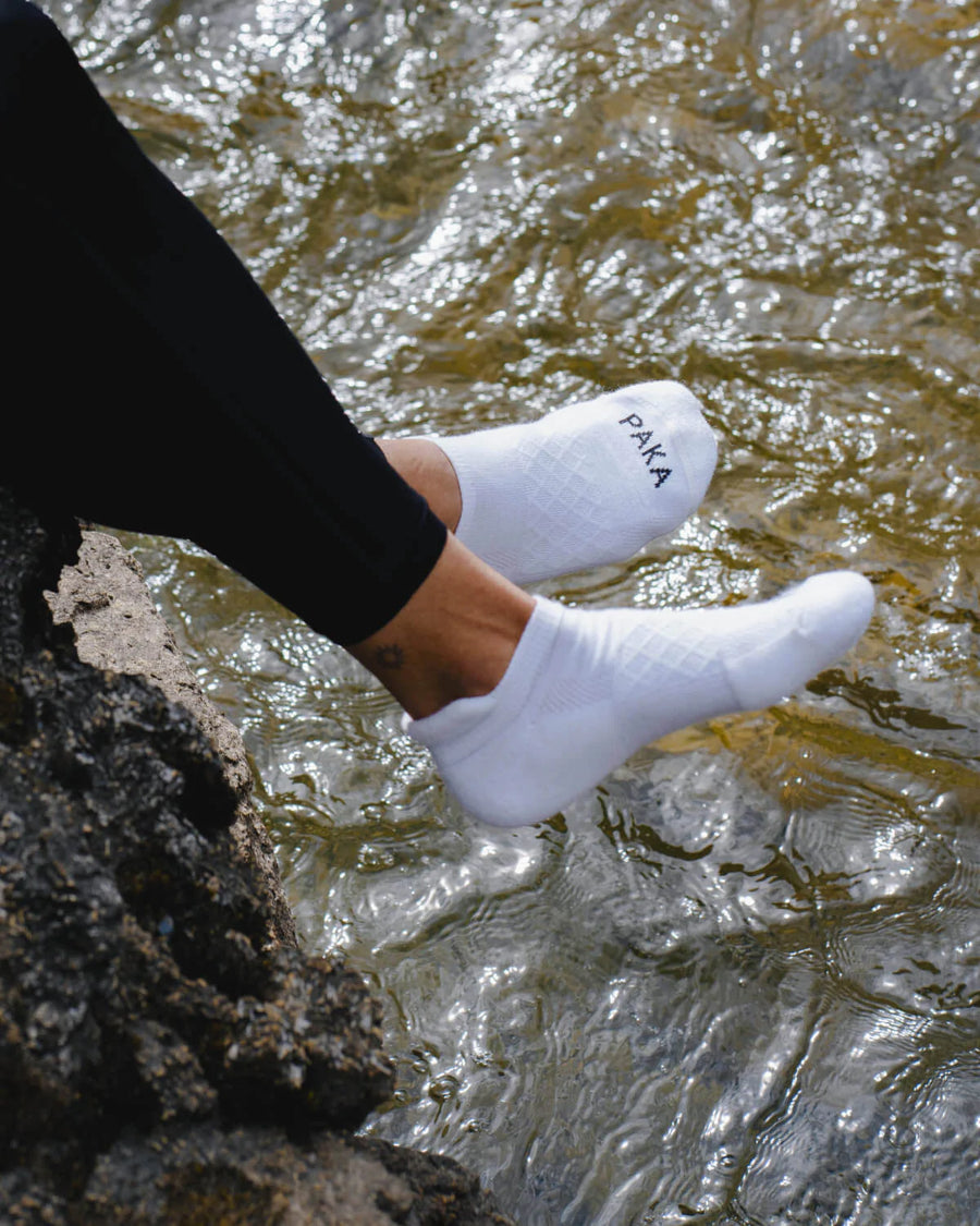 Woman dangling feet over river wearing white alpaca wool ankle socks