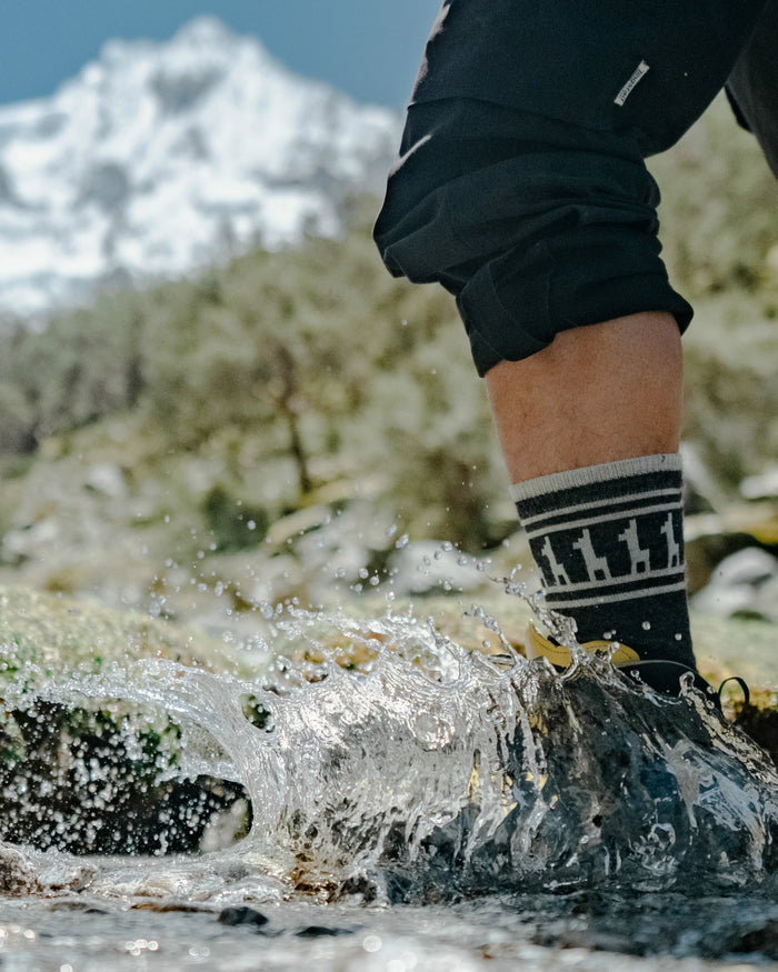 Man’s Leg Stepping Through Stream with Hiking Boot and Costa Charcoal / Dark Grey Alpaca Wool Thermal Sock with Alpaca Print Design – PAKA Apparel